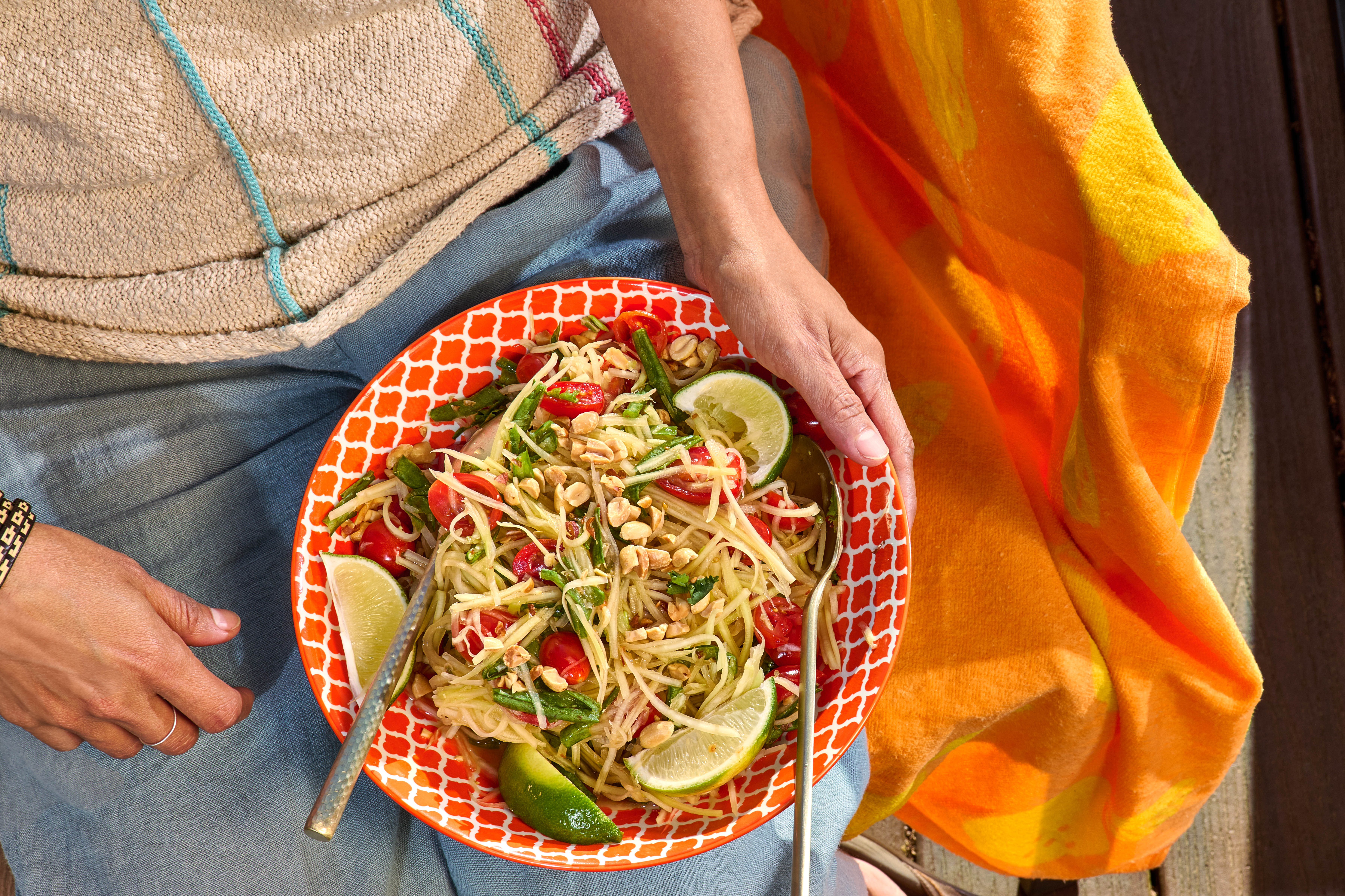 A big bowl of papaya salad, balanced on someone’s lap.