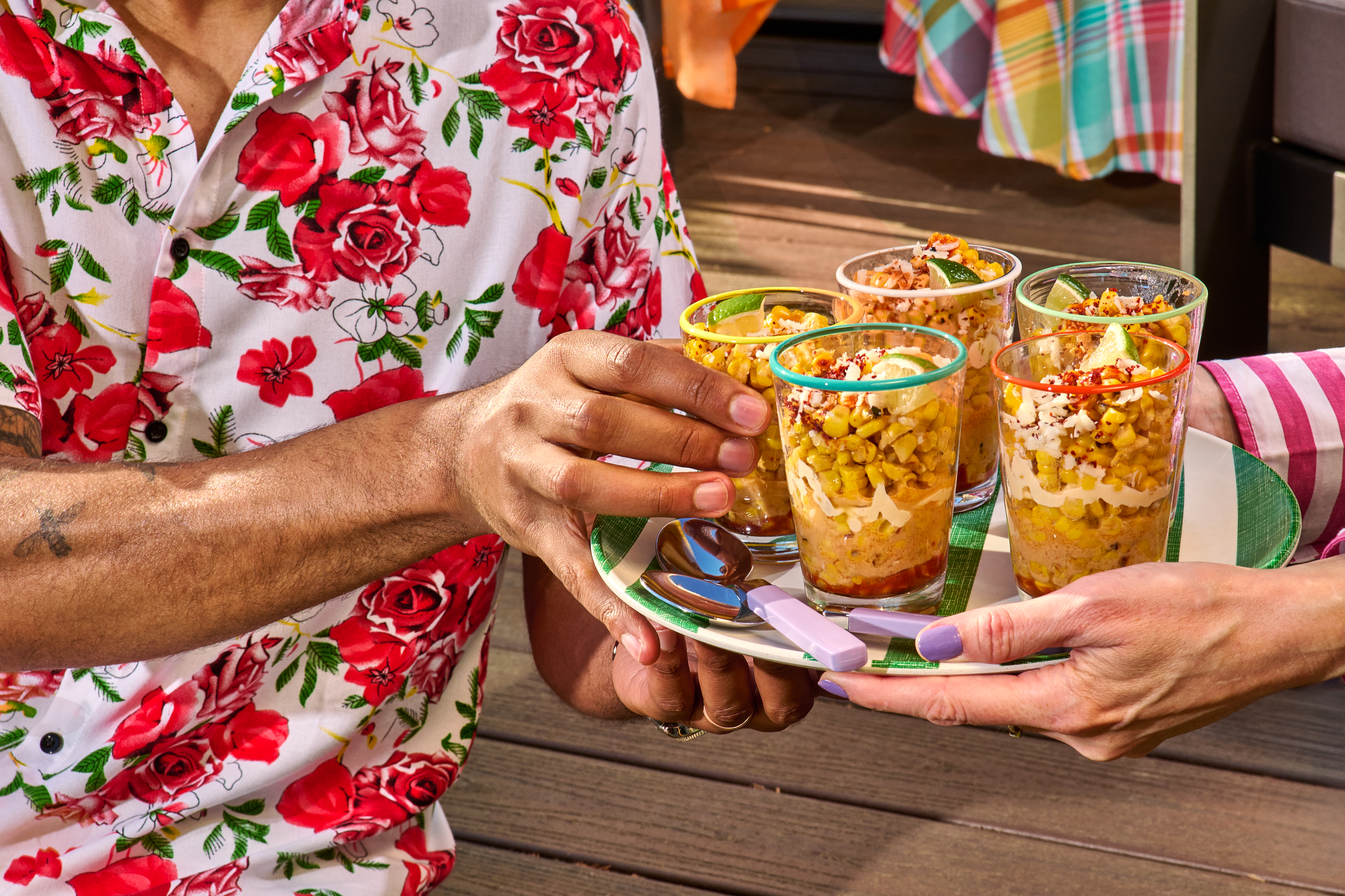 Glasses of esquite are served to party guests from a colorful plate.