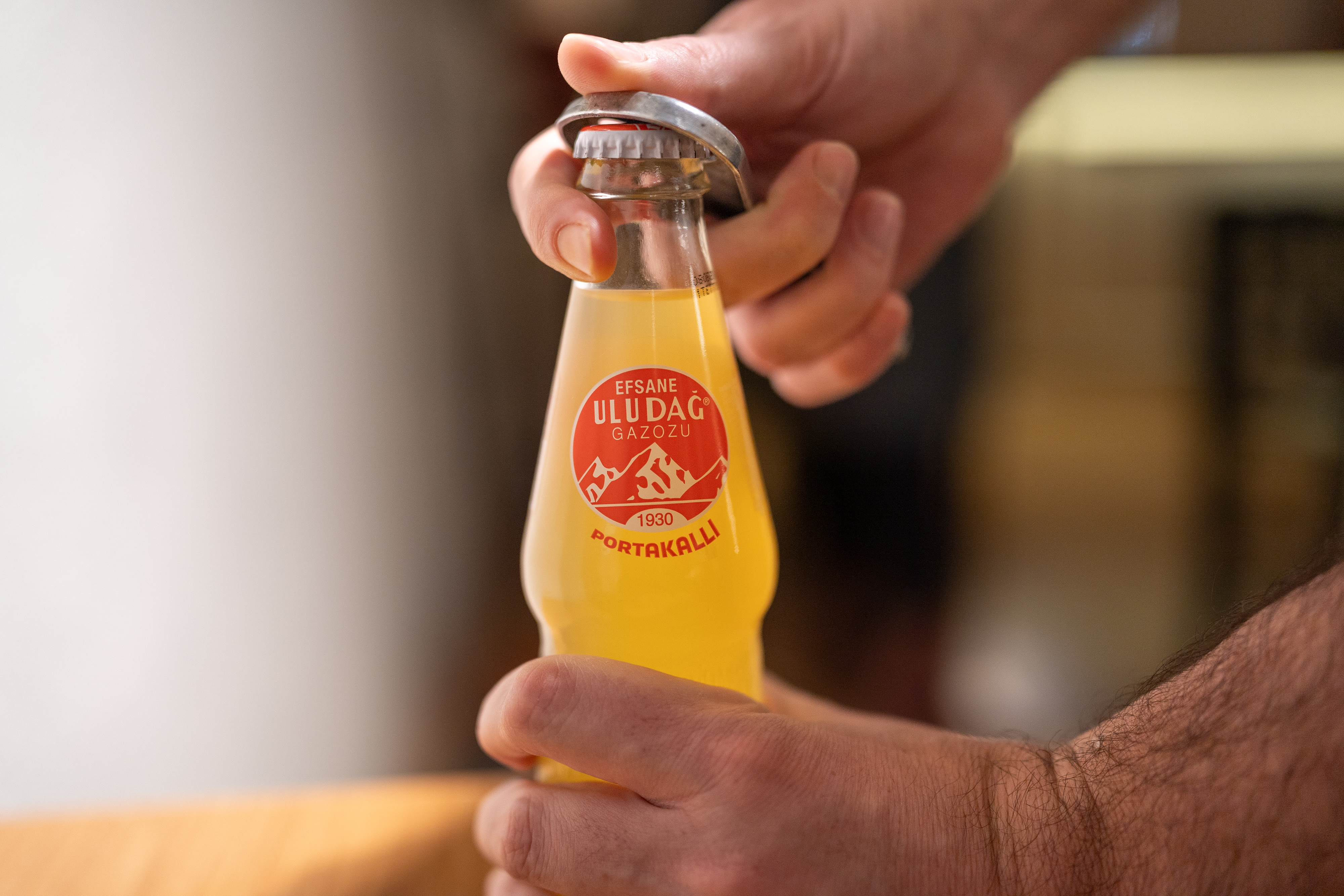 A person opens a bottle of Uludağ Gazoz with a bottle opener.