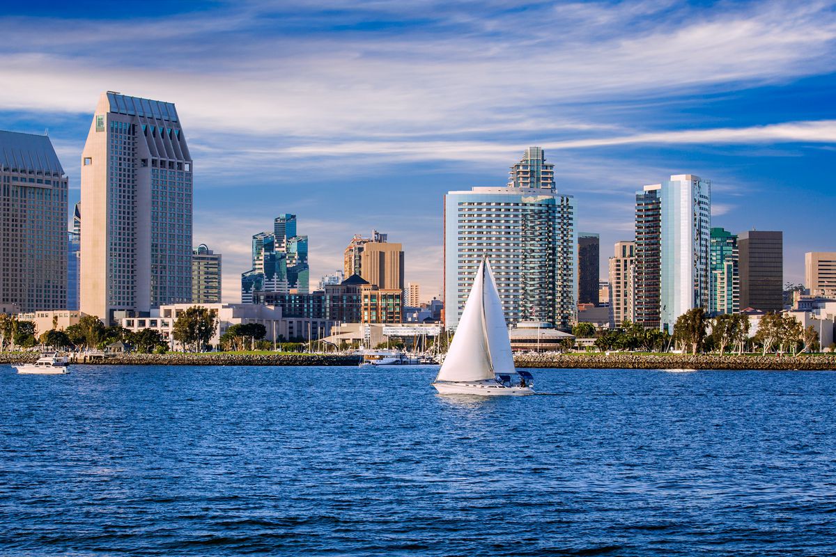 A sailboat in water in from of the buildings that make up the downtown San Diego skyline.