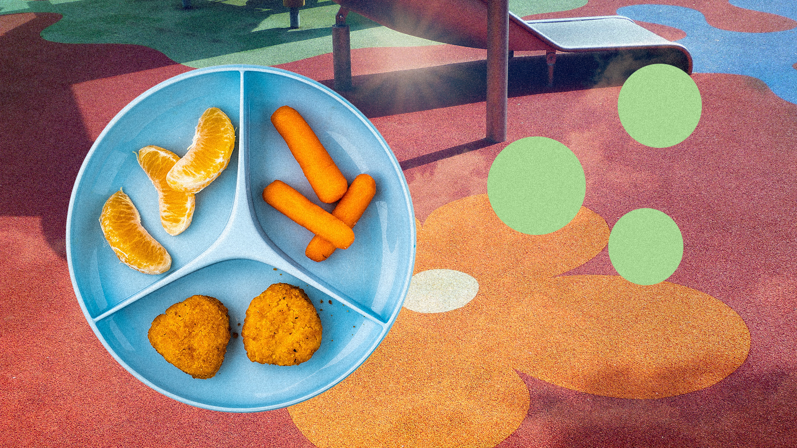 A divided plate with chicken nuggets, baby carrots and citrus slices on a background of colorful a playground surface